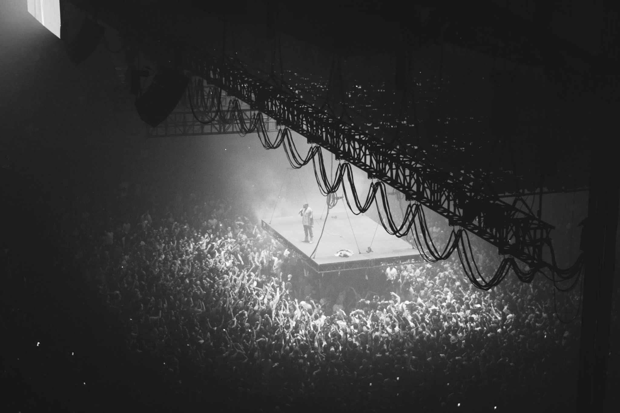 a singer on a stage holding a microphone in a dark crowded auditorium. He is in the spotlight.